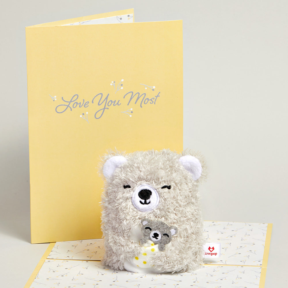 stuffed bear in front of a Mother's Day cards that says "Love You Most"